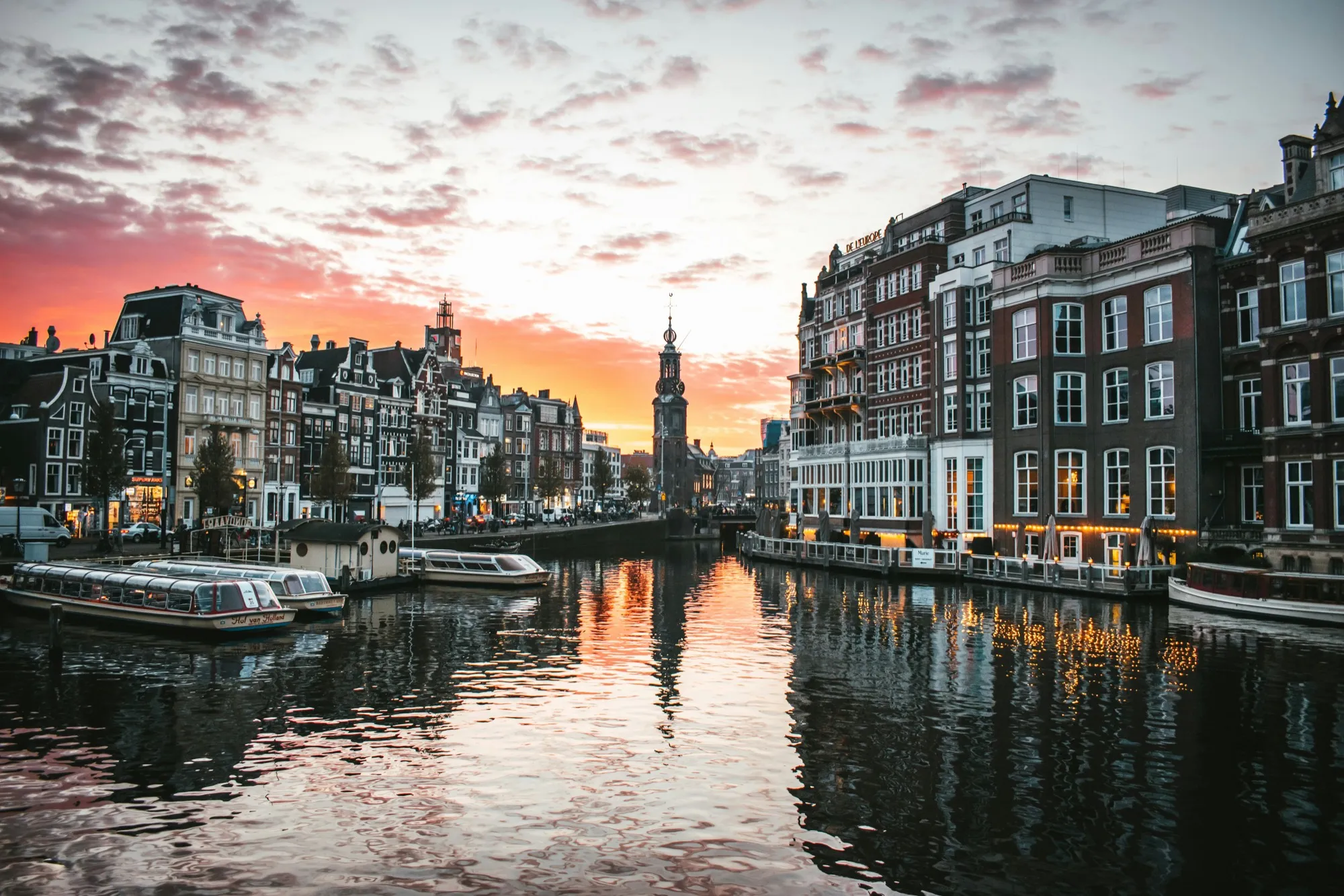 An Amsterdam canal at sunset, tour boats moored along the quay in front of the Munttoren.