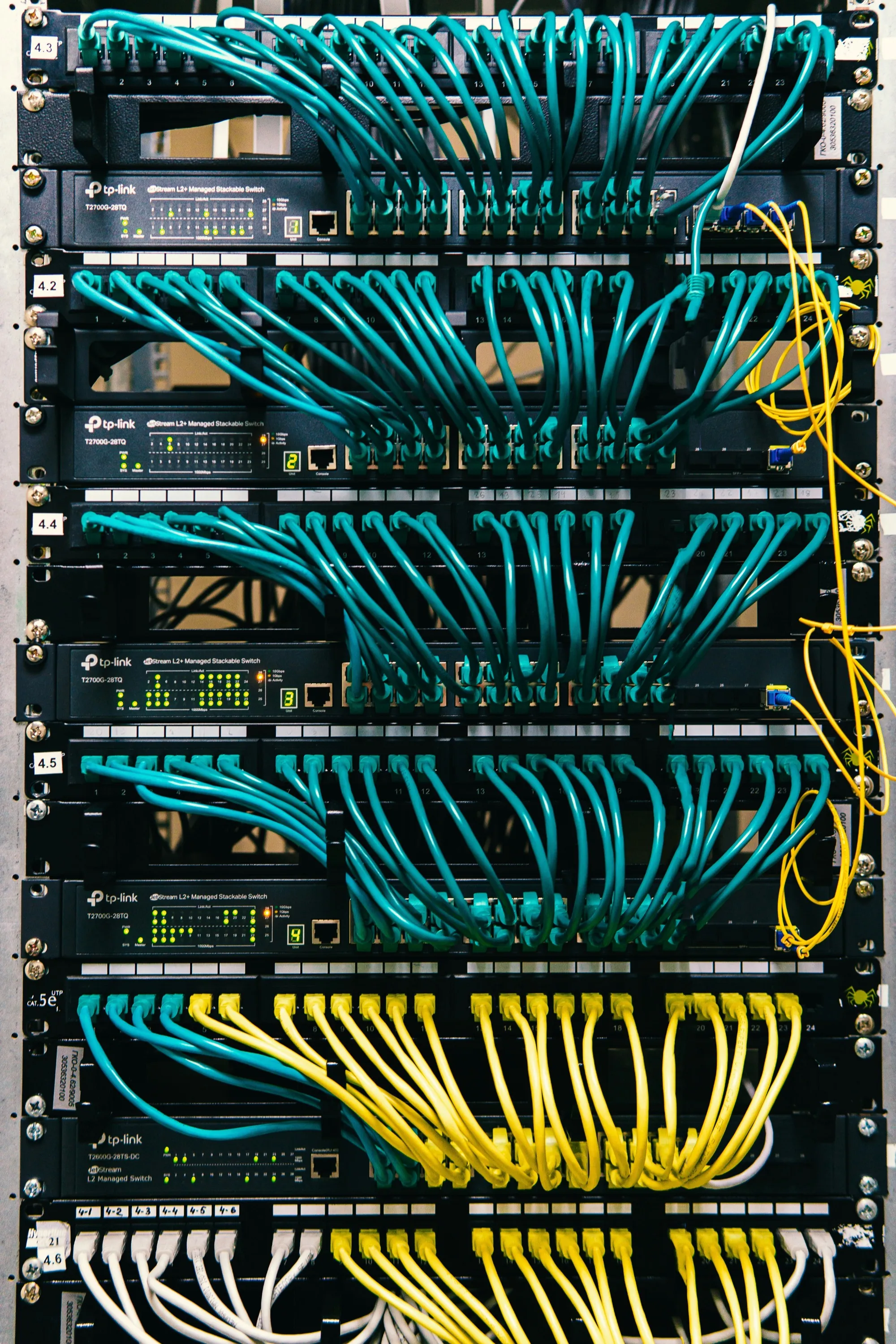 A network rack: patch panels and managed switches, with ranks of teal ethernet cables looped between them.