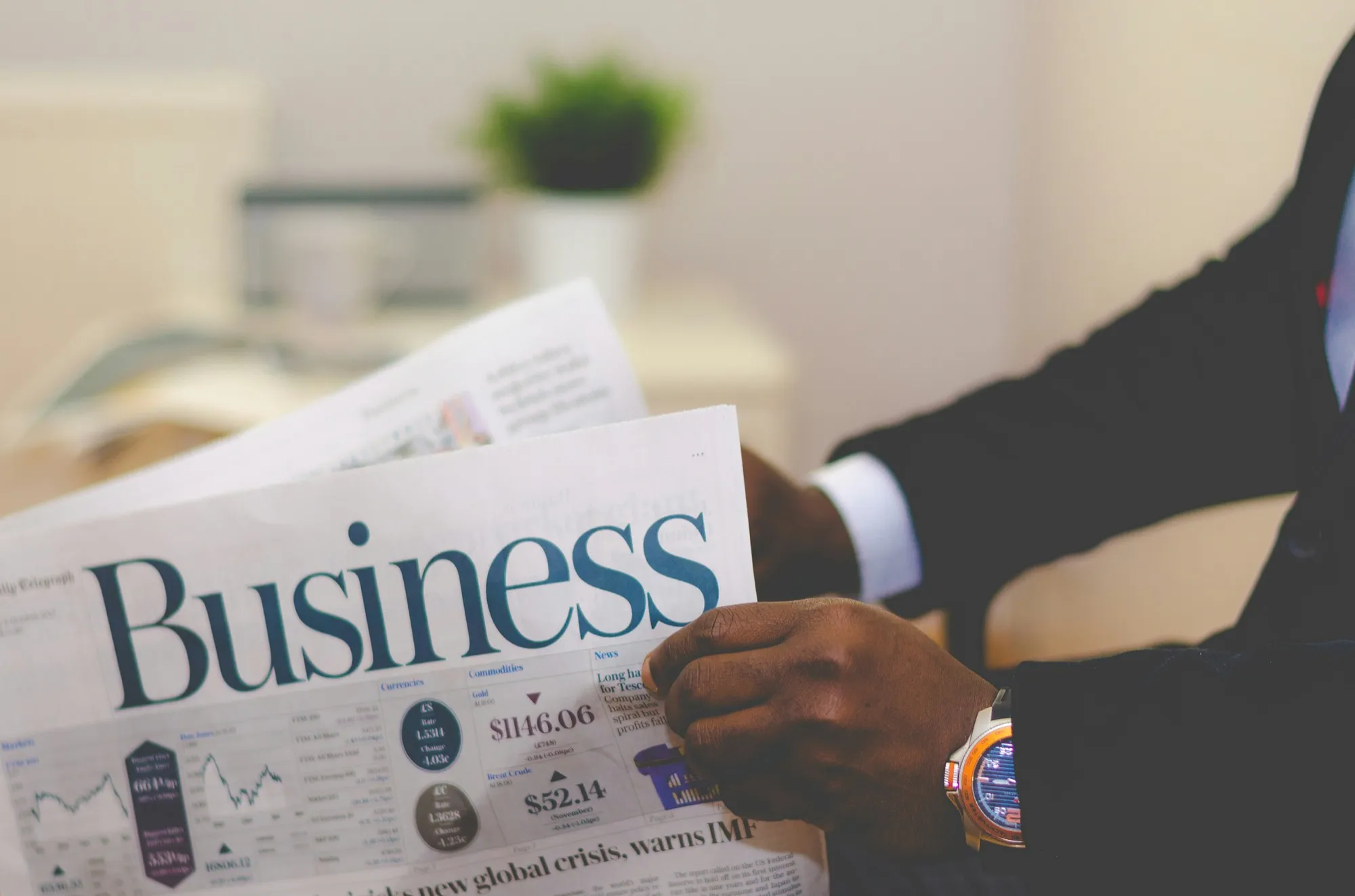 Someone in a suit reading the business pages of a newspaper, market tables in view.